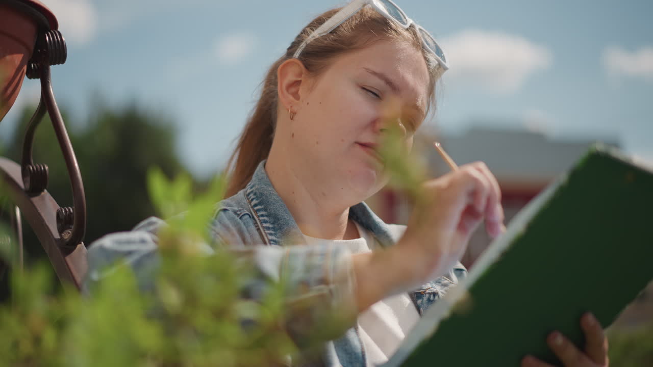 Una donna esamina le piante. Una ricercatrice documenta diligentemente i dettagli delle piante all'esterno. Un individuo analizza e registra attentamente le caratteristiche delle piante durante una sessione di ricerca soleggiata all'aperto.