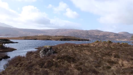 Langsames-Schwenken-Einer-Landschaft-Aus-Lewis-Gneis-Mit-Blick-Auf-Das-Wasser-Von-Loch-Inver,-Inseln-Mit-Bäumen-Und-Büschelgräsern-Im-Hochland-Von-Schottland,-Großbritannien