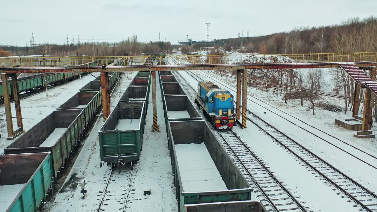 A blue freight train arrives at its destination amid a multitude of containers on a winter day. Aerial view.