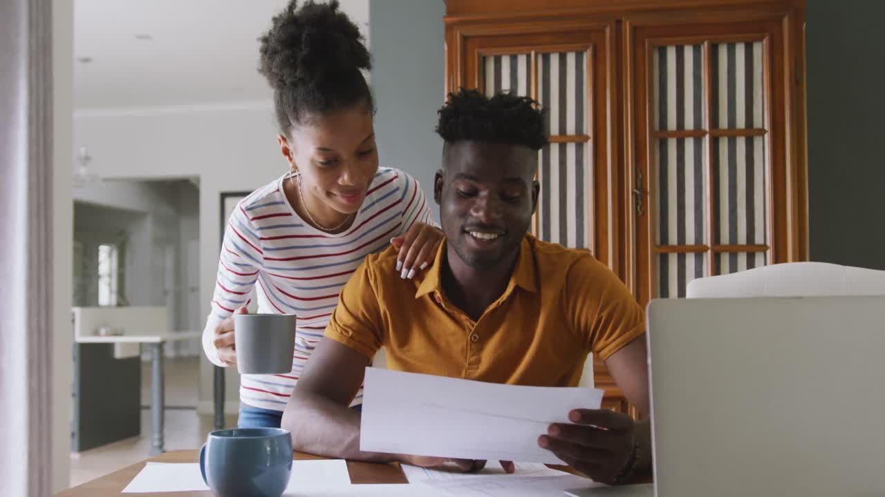 Video of happy african american couple using laptop, paying bills