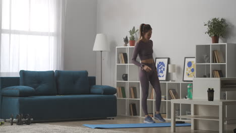 joven está entrenando sola en la sala de estar y tomando descansos de entrenamiento en casa durante el auto-aislamiento y la cuarentena manteniendo la forma y la salud