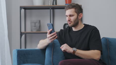 el joven se alegra al ganar, leyendo el mensaje en el teléfono inteligente sentado en casa, alegría frenética