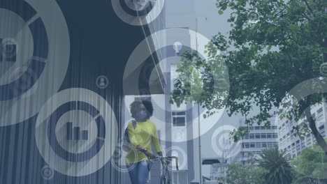Animation-Von-Mediensymbolen-über-Einer-Afroamerikanischen-Frau-Mit-Gesichtsmaske,-Die-Fahrrad-In-Der-Stadtstraße-Fährt