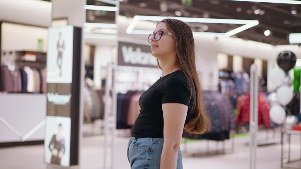 joven con gafas caminando en un centro comercial con luces bokeh en el fondo, rodeada de exhibiciones de tiendas con ropa de moda, iluminación brillante y entorno comercial moderno