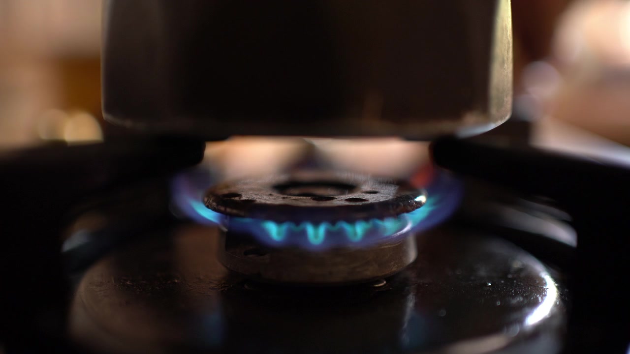 A hand sparks a lighter to ignite a gas stove burner beneath a coffee pot, Close-up Shot