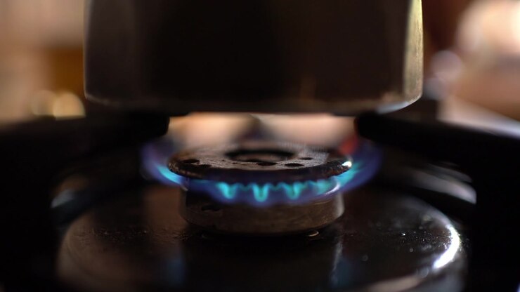 A hand sparks a lighter to ignite a gas stove burner beneath a coffee pot, Close-up Shot