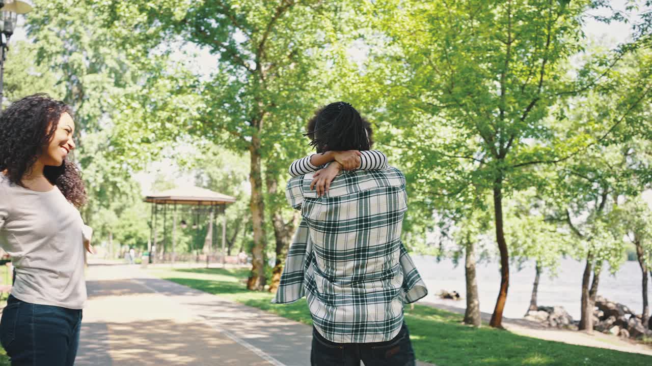 어머니와 아버지는 작은 딸과 함께 공원에서 산책합니다. 남자는 소녀를 둘러싸고, 친절한 가족은 주말에 어리석습니다.