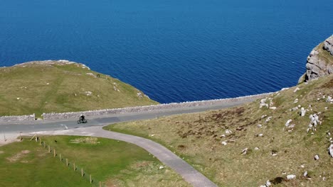 tourist riding mountain bike along scenic green mountain country road overlooking gorgeous blue irish sea pan left