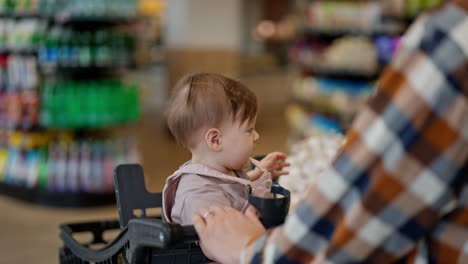 Close-up-of-a-little-girl-baby-sitting-in-a-cart-during-a-trip-to-the-supermarket-and-shopping-with-her-mom