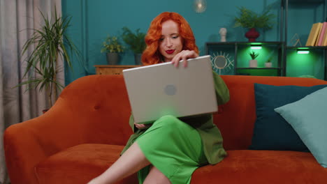Redhead-girl-freelancer-starts-working-on-laptop,-sends-messages,-makes-online-purchases-at-home
