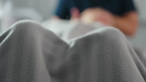 woman covered in striped grey blanket lying on massage bed in bright spa room with faint blurred image of therapist massaging her during relaxing wellness session in serene tranquil environment