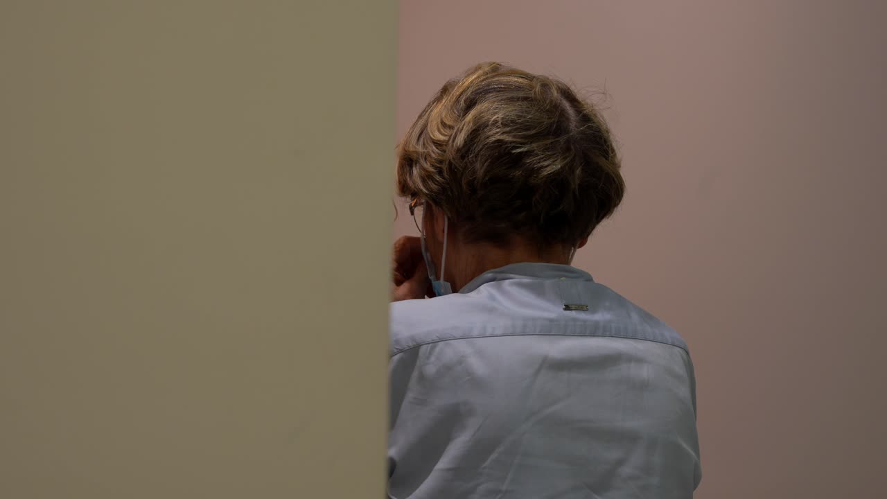 Rear view of dentist assisting elderly woman removing hygiene cap, mask remains on