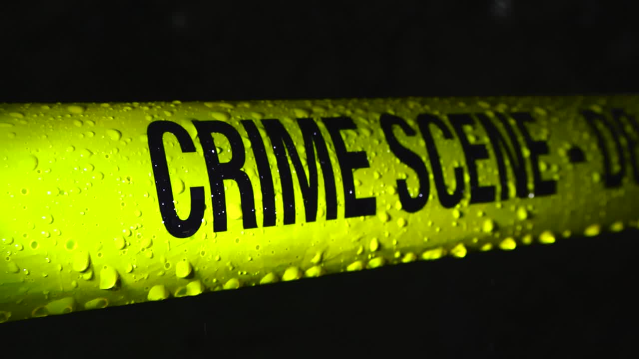 Yellow colored police line Crime Scene forensics investigation tape pulled in front of a pitch black or dark night forest area during heavy rainfall with raindrops fallin and moving on the ribbon tape
