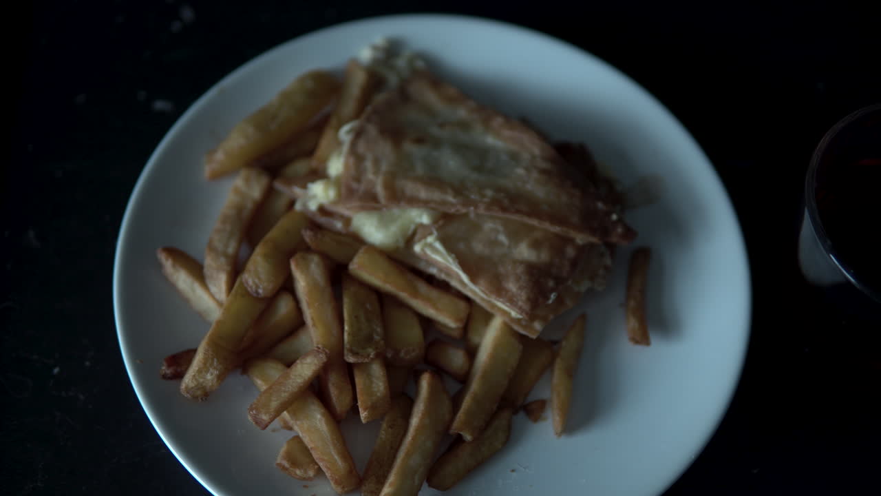 Hvit tallerken med pommes frites og nachos og et glass te på svart arbeidsplate, panne