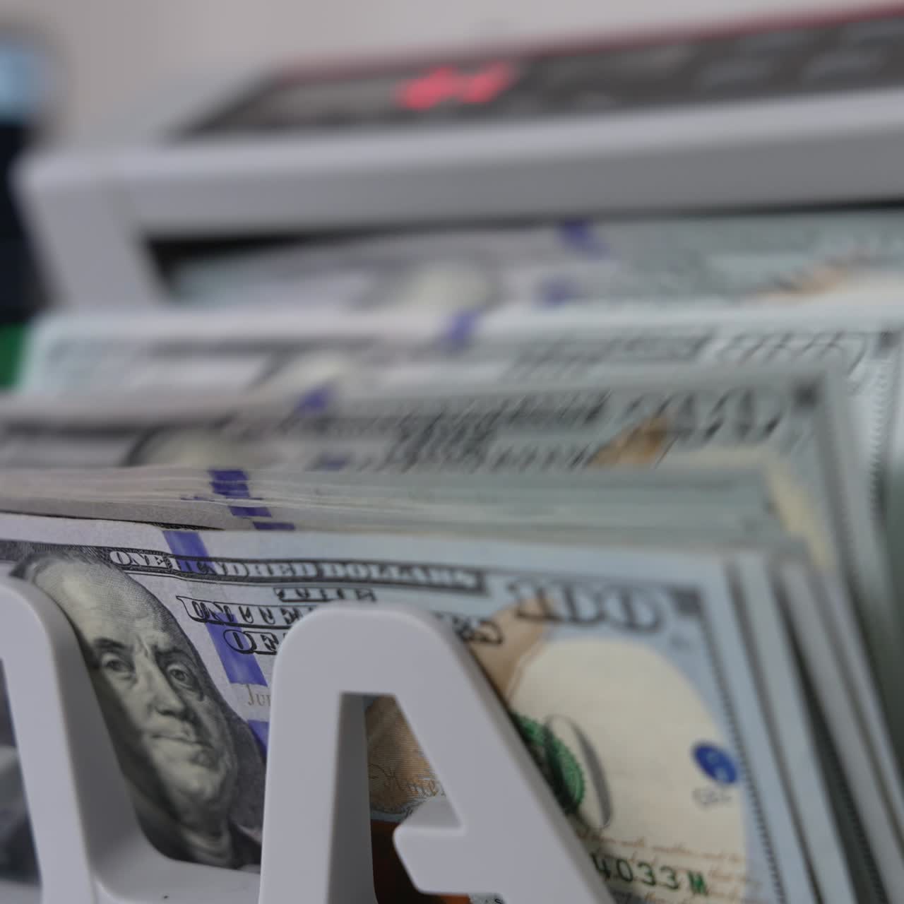 Notes with Benjamin Franklin portraits fall on the holder of cash counting machine. Close up. Blurred background