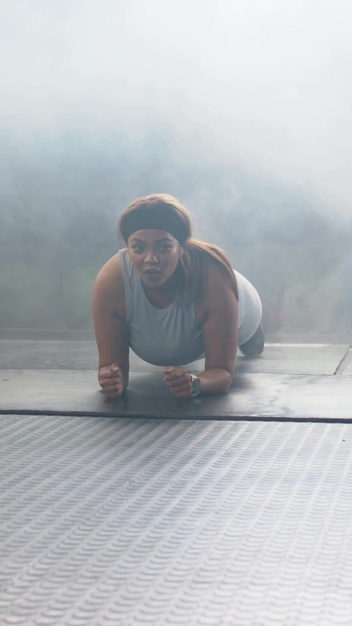 Video verticale: Donna con canotta che inizia la routine, mantenendo la posizione del plank sugli avambracci su un tappetino da palestra, con orologio visibile.