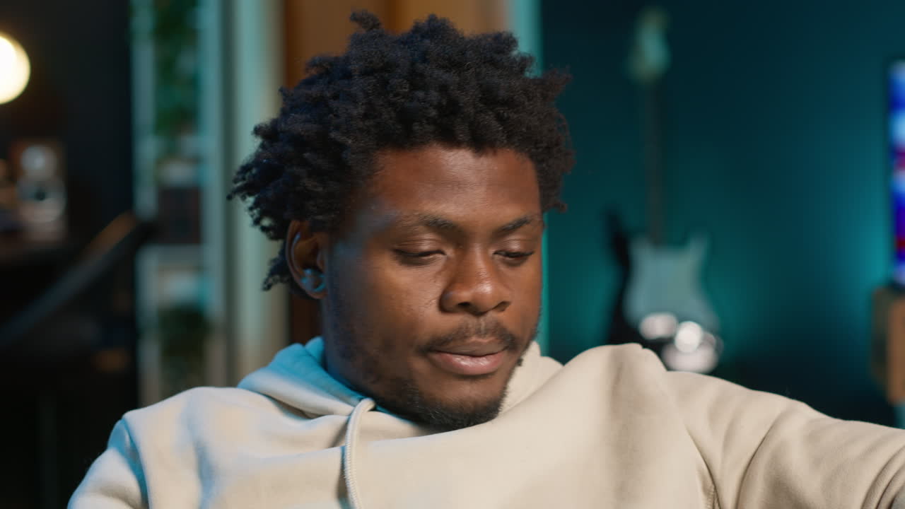 African american man suffering from a migraine and illness, sitting on couch at home and feeling overworked. Concerned young adult struggling with pain, tired and anxious guy. Camera B.