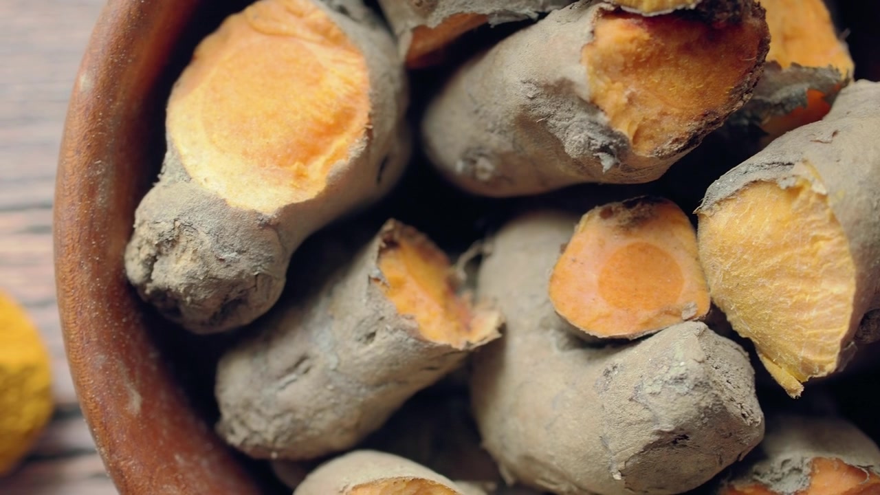 Radici di curcuma fresche in una ciotola con curcuma in polvere