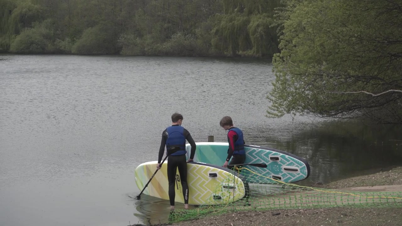 Venner søsætter stand up paddleboards på en fredelig, beskyttet sø. Filmet i 4k