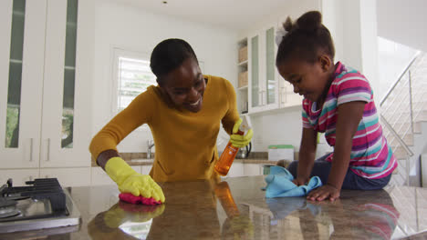 african american mother and daughter cleaning countertops and laughing in kitchen