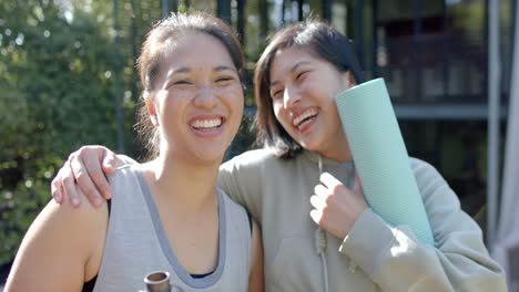 Felices-Amigas-Asiáticas-Con-Colchonetas-De-Ejercicio-Y-Botella-De-Agua-Riéndose-En-La-Terraza,-Cámara-Lenta