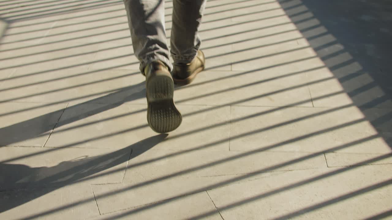 A man is seen ascending concrete stairs, with long shadows from sunlight on a striped pattern cast on the steps