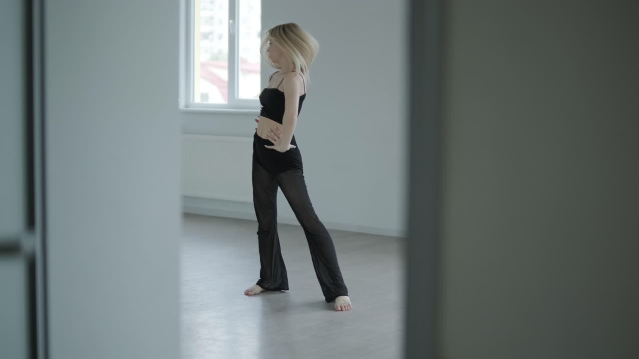 Ballerina in abiti neri che esegue danza contemporanea. Movimenti fluidi e aggraziati in una stanza bianca. Coreografia di balletto moderno.