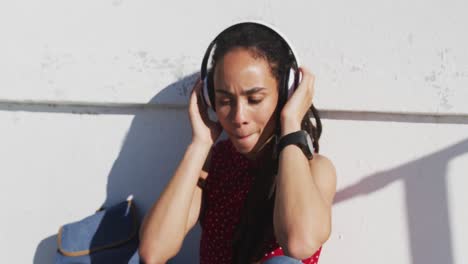 African-american-woman-wearing-headphones-and-listening-to-music-on-promenade-by-the-sea