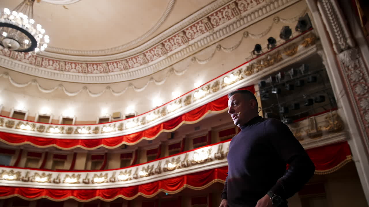 Man is giving interview in the opera house. Middle-aged actor talking to someone while standing on stage on classical theatre background.