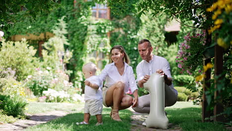 caucasian family celebrating first birthday of their little baby. dad taps his hand by the balloon un the shape of number one. beautiful garden at backdrop.