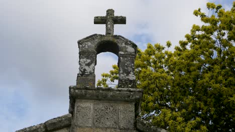 low angle looking up at carved stone cross and moss lichens and yellow green blossoms at chapel of san vitoiro