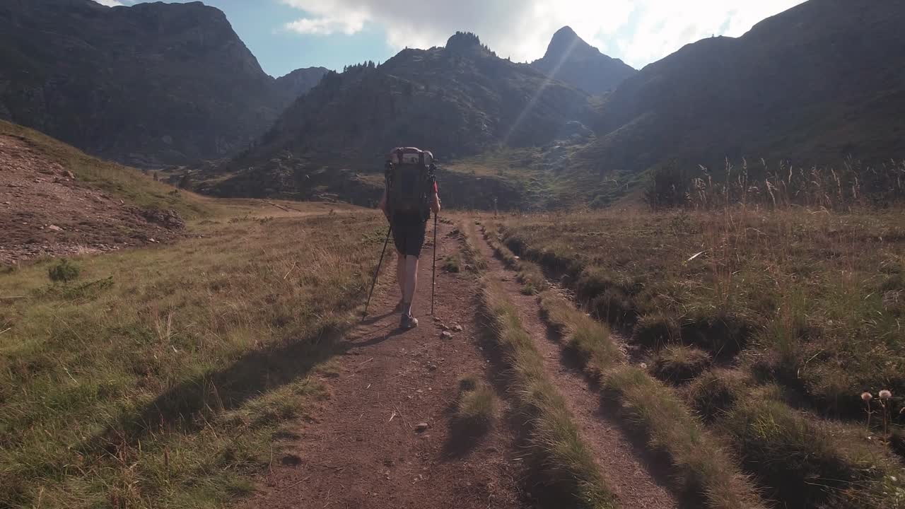 vista trasera de un excursionista con una gran mochila caminando hacia el pico de la montaña en la soleada tarde de verano-1
