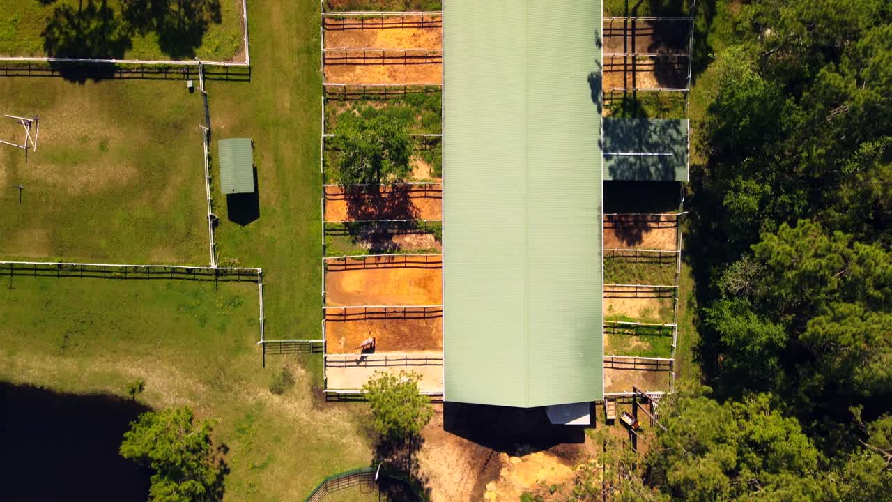 A drone flies over a horse barn looking straight down at it