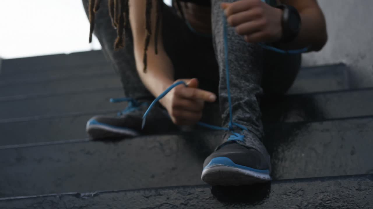 Front view of young African American woman tying shoelaces in the city 4k