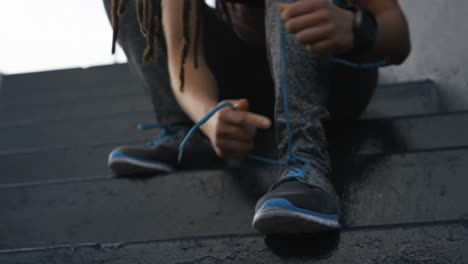 Front-view-of-young-African-American-woman-tying-shoelaces-in-the-city-4k