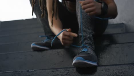 Vista-Frontal-De-Una-Joven-Afroamericana-Atando-Cordones-De-Zapatos-En-La-Ciudad-4k