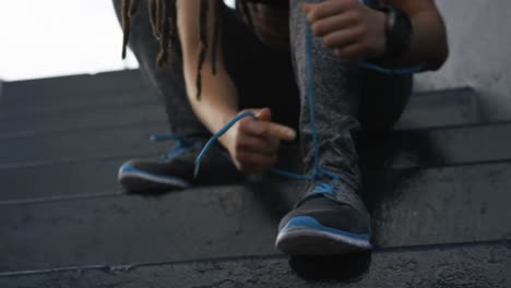 vista frontal de una joven mujer afroamericana atando cordones de zapatos en la ciudad 4k