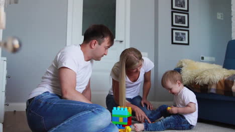 happy family dad mom and baby 2 years playing lego in their bright living room. slow-motion shooting happy family