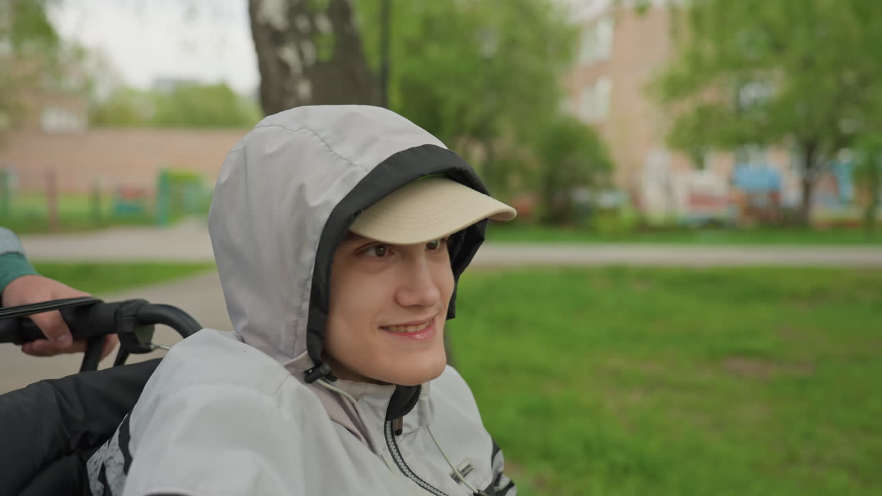 Smiling Adolescent With Wheelchair Outdoors, Cheerful Young Person Sitting In Mobility Device Surrounded By Nature, Brighteyed Teenager Enjoying Peaceful Day In Park With Support And Happiness