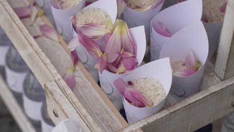 close up of wedding rice cones with pink flower petals arranged in a wooden crate