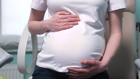 camera focuses on pregnant woman's hands touching her belly in the medical consultation