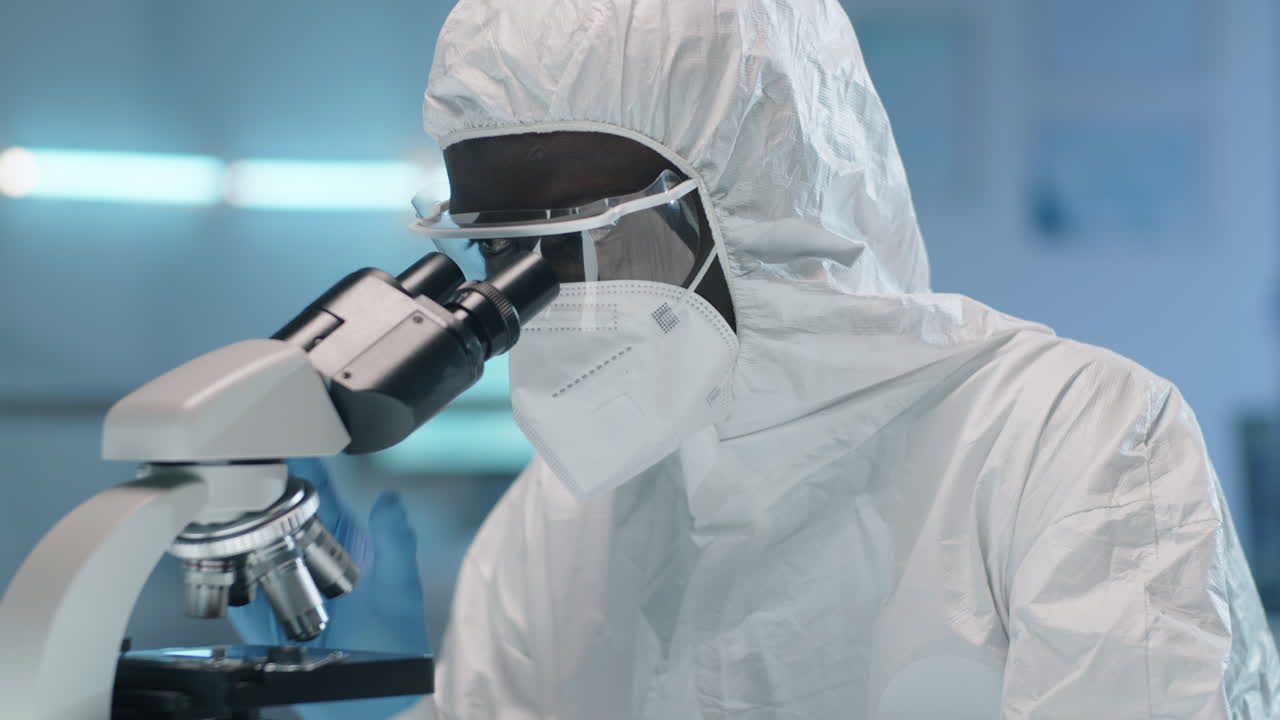 保護服を着たアフリカ系アメリカ人科学者が ⁇ 微鏡を使って