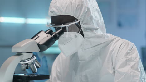 african american scientist in protective suit using microscope