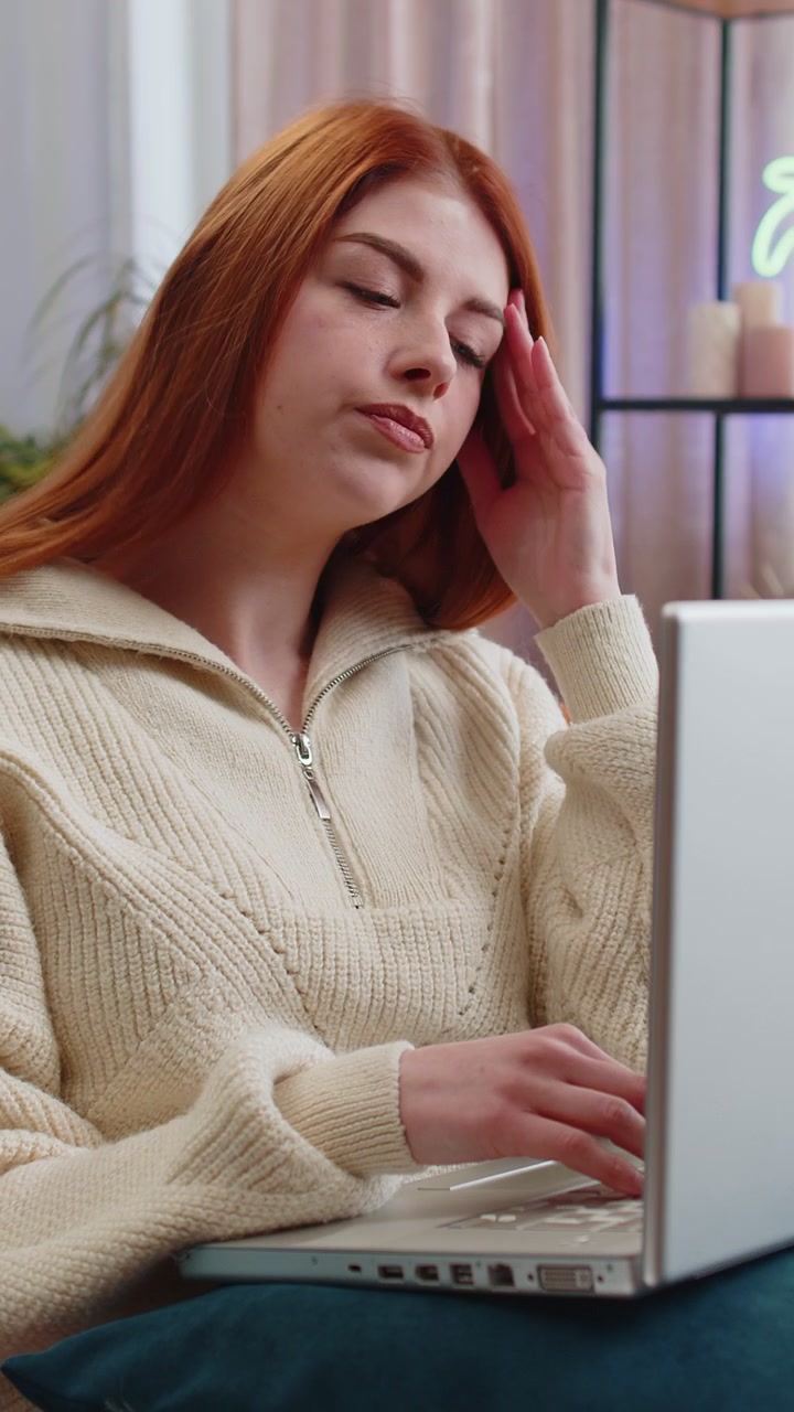 Una giovane donna stanca, freelance, usa un portatile, soffre di mal di testa, di problemi di tensione e di stress da emicrania.