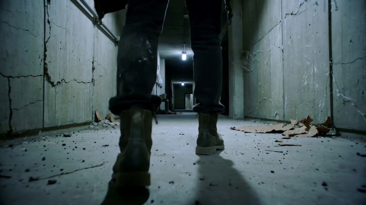 Vertical video: Walking man in rolled jeans, ankle boots, heading toward lit doorway, bulb guiding