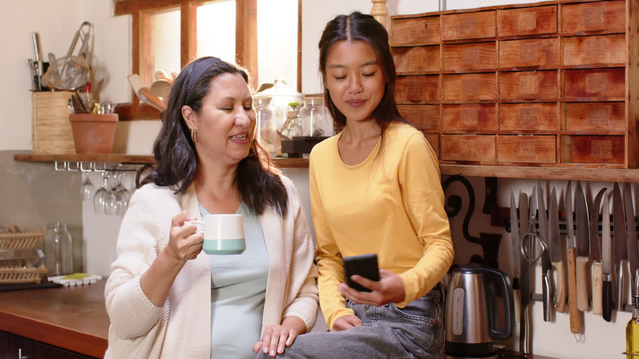 Multiracial young woman taking selfie with grandma in cozy kitchen, both smiling warmly, at home
