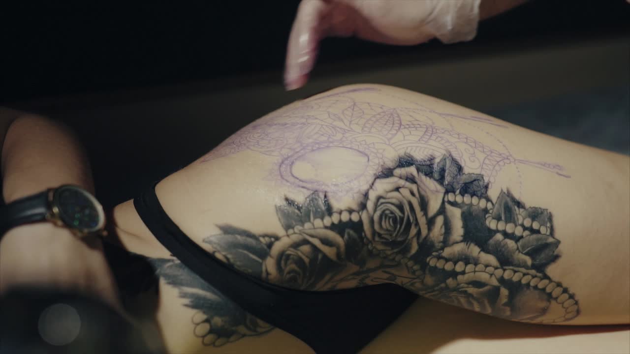 Tattoo artist working on a thigh tattoo