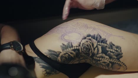 artista del tatuaje trabajando en un tatuaje en el muslo