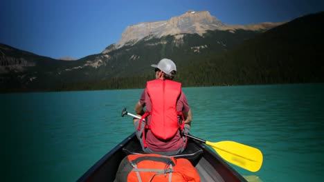 Rear-view-of-young-caucasian-man-rowing-boat-on-a-turquoise-river-in-the-sunshine-4k