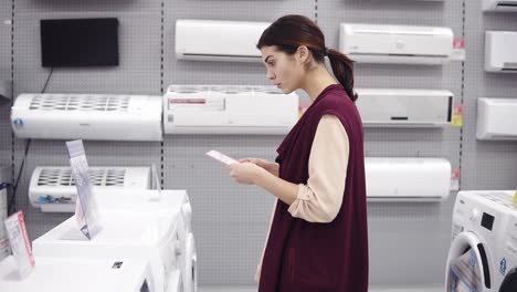 cliente femenino comprobando la etiqueta de precio mientras elige la lavadora en la tienda de electrodomésticos. compra de nuevos equipos domésticos